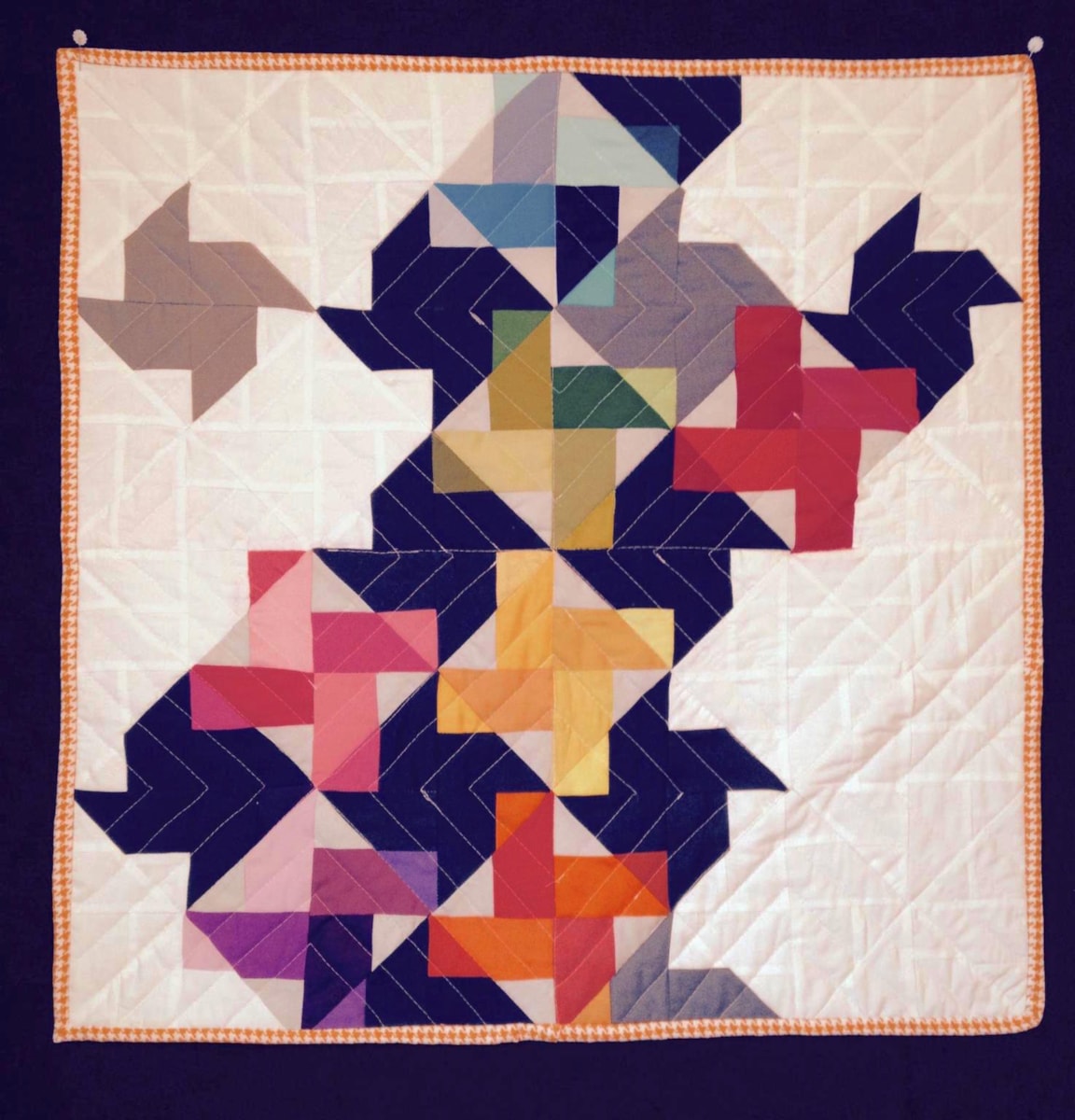 By Jill Kofton. I made verston #2, Scrappier 25.5" x 25.5." My past two quilts have used only solids. So, I had a large variety of scraps to choose from. I wanted to do a play off the pinwheel feel while adding a modern twist. This I carried over to the quilt back where I did one page pinwheel in warm and color colors as a single large block on back (not pictured. The piece was bound with an orange/white houndstooth.